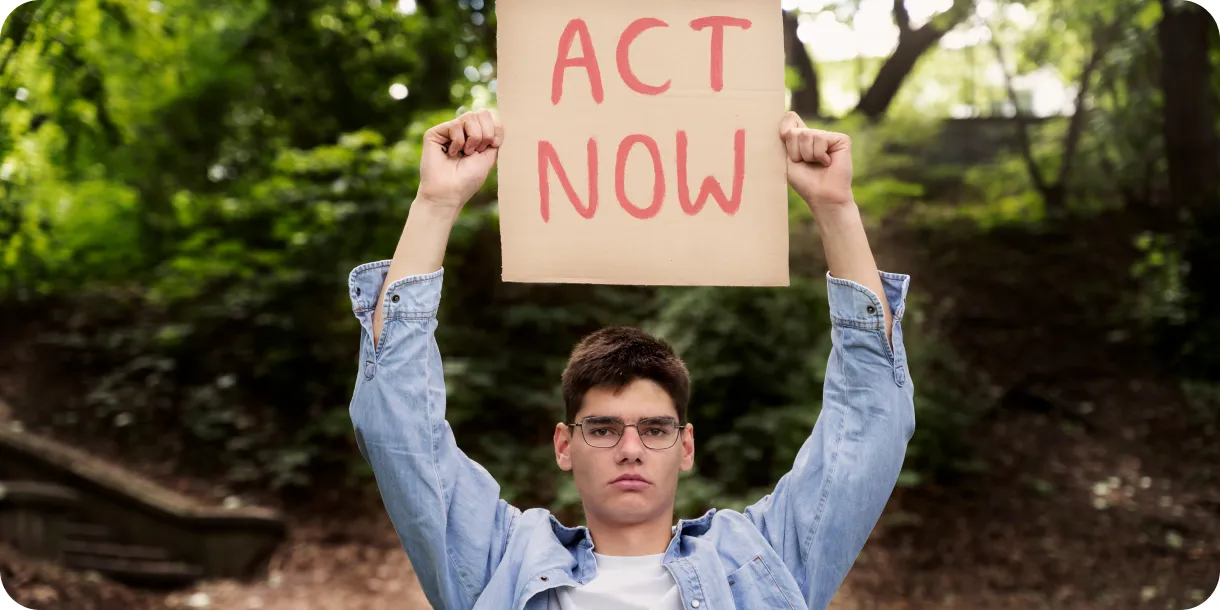A person holding up an "Act Now" protest sign in a forest